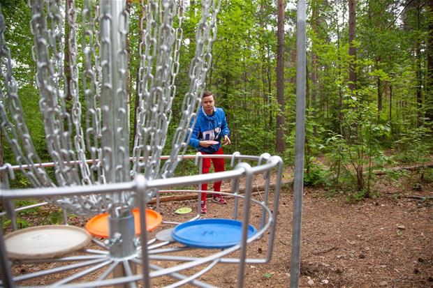 Frisbeegolf maali ja mies heittämässä frisbeetä